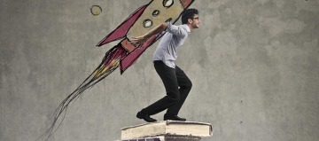 man with rocket on his back standing on a pile of books